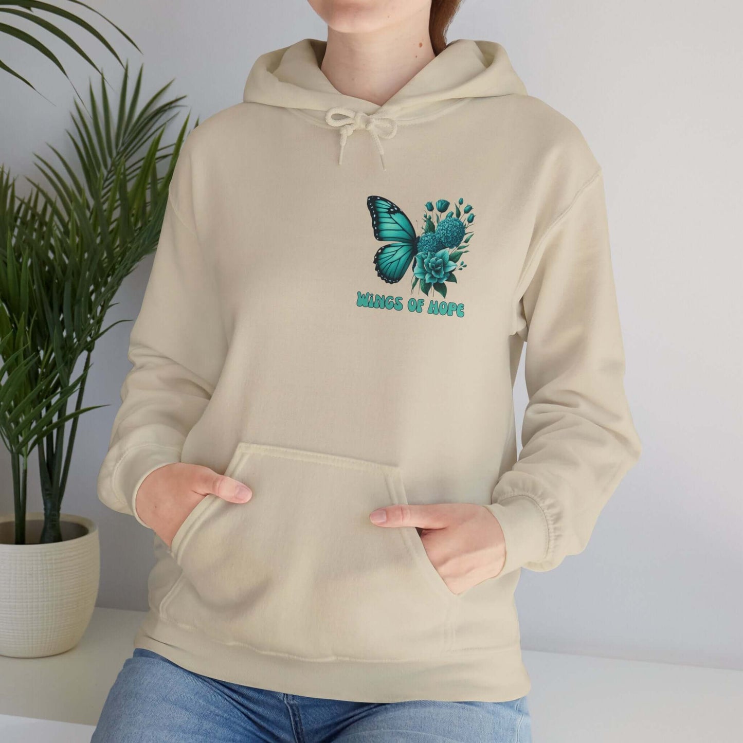 Person wearing "Wings Of Hope" Butterfly and Flowers Hoodie with soft beige fabric, showcasing butterfly and floral design, standing indoors