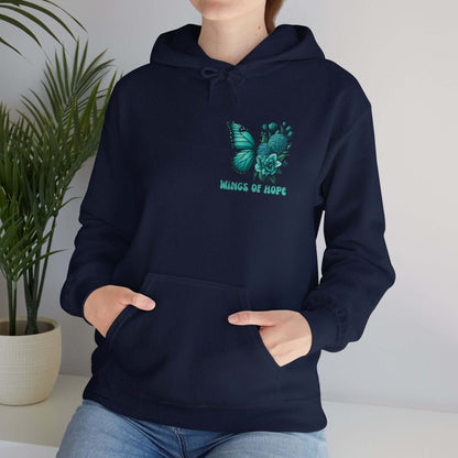 Woman wearing black hoodie with butterfly and flowers design and "Wings of Hope" text, standing near a green plant.