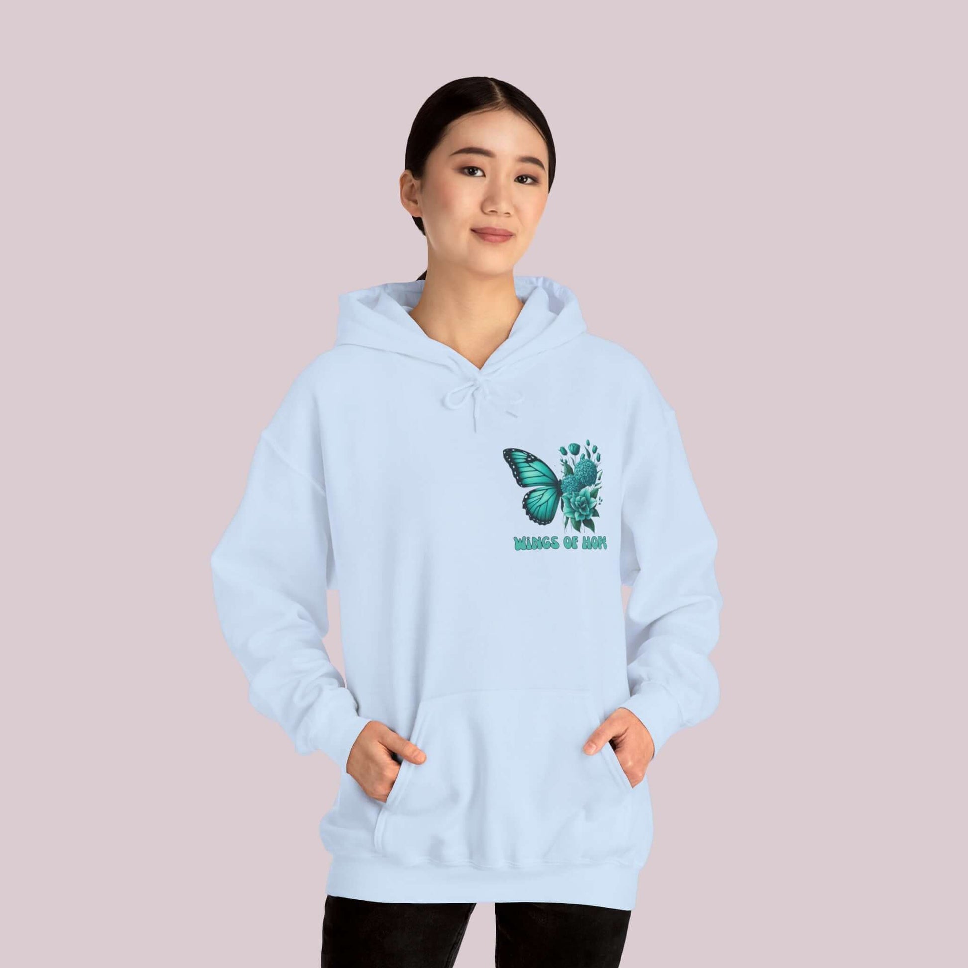 Woman wearing "Wings Of Hope" Butterfly and Flowers Hoodie, light blue, cozy and stylish, soft high-quality fabric, positive message.